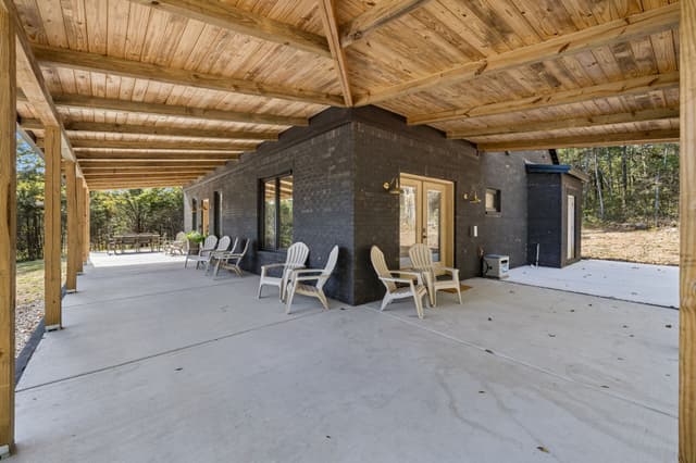 The Salem House wraparound porch with exposed timber beams, Adirondack chairs, and outdoor dining beside the woods.