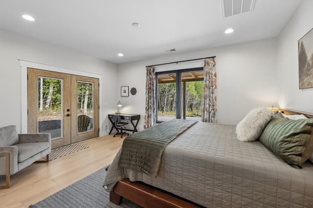 The Salem House master suite with a king bed, soft green bedding, and doors opening toward the wooded porch.
