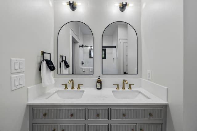 The Salem House bathroom vanity with twin sinks, arched mirrors, brass fixtures, and fluted cabinetry.