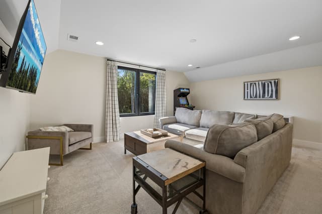 The Salem House loft with a sectional sofa, television, arcade game, and a window overlooking the woods.