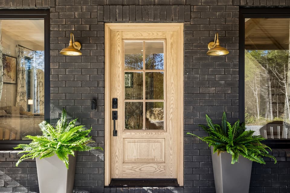 The Salem House entrance with a natural wood door, brass lights, and lush potted ferns against dark brick.